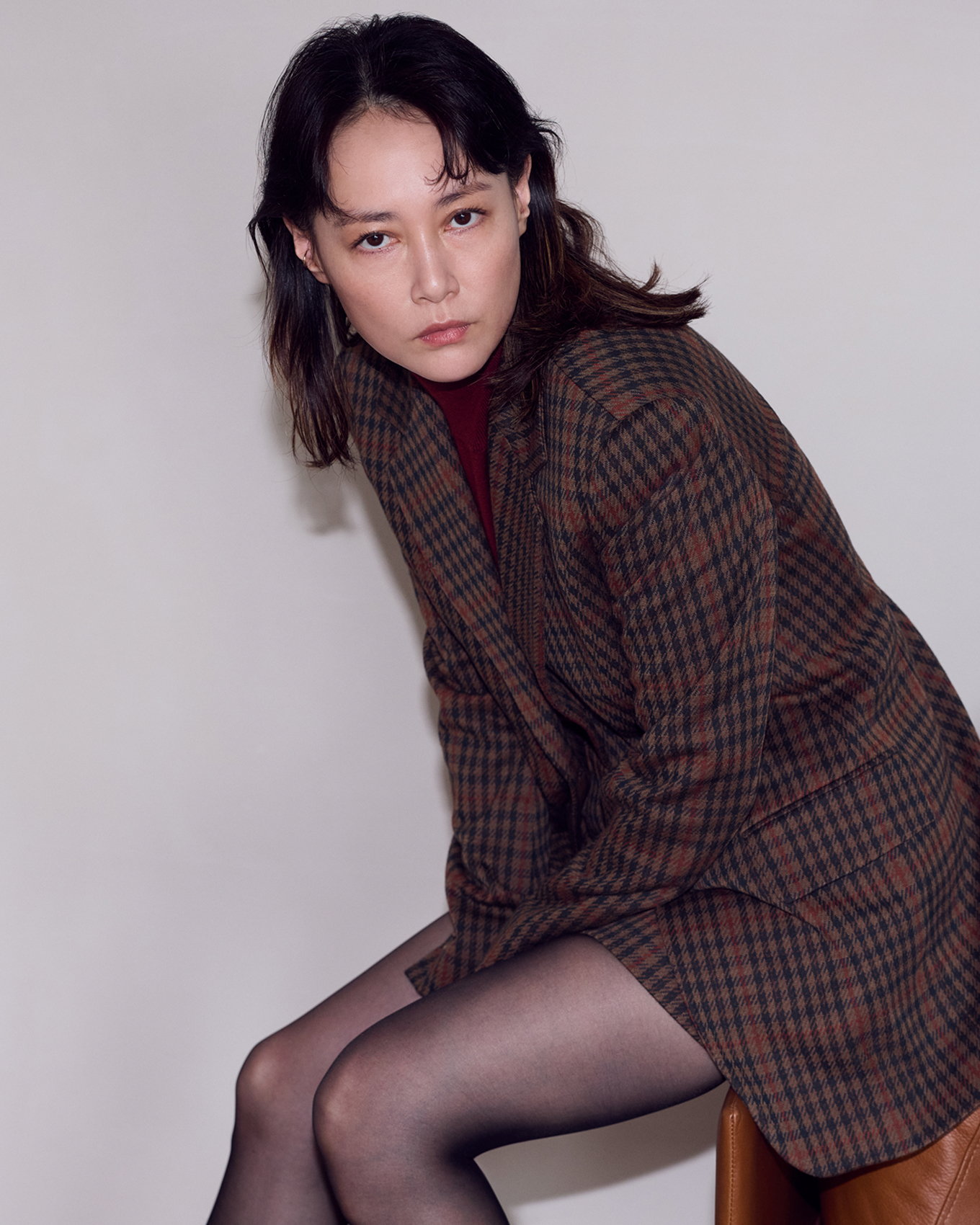 チェック柄のシングルブレストジャケットをまとい、椅子に腰掛ける菊地凛子